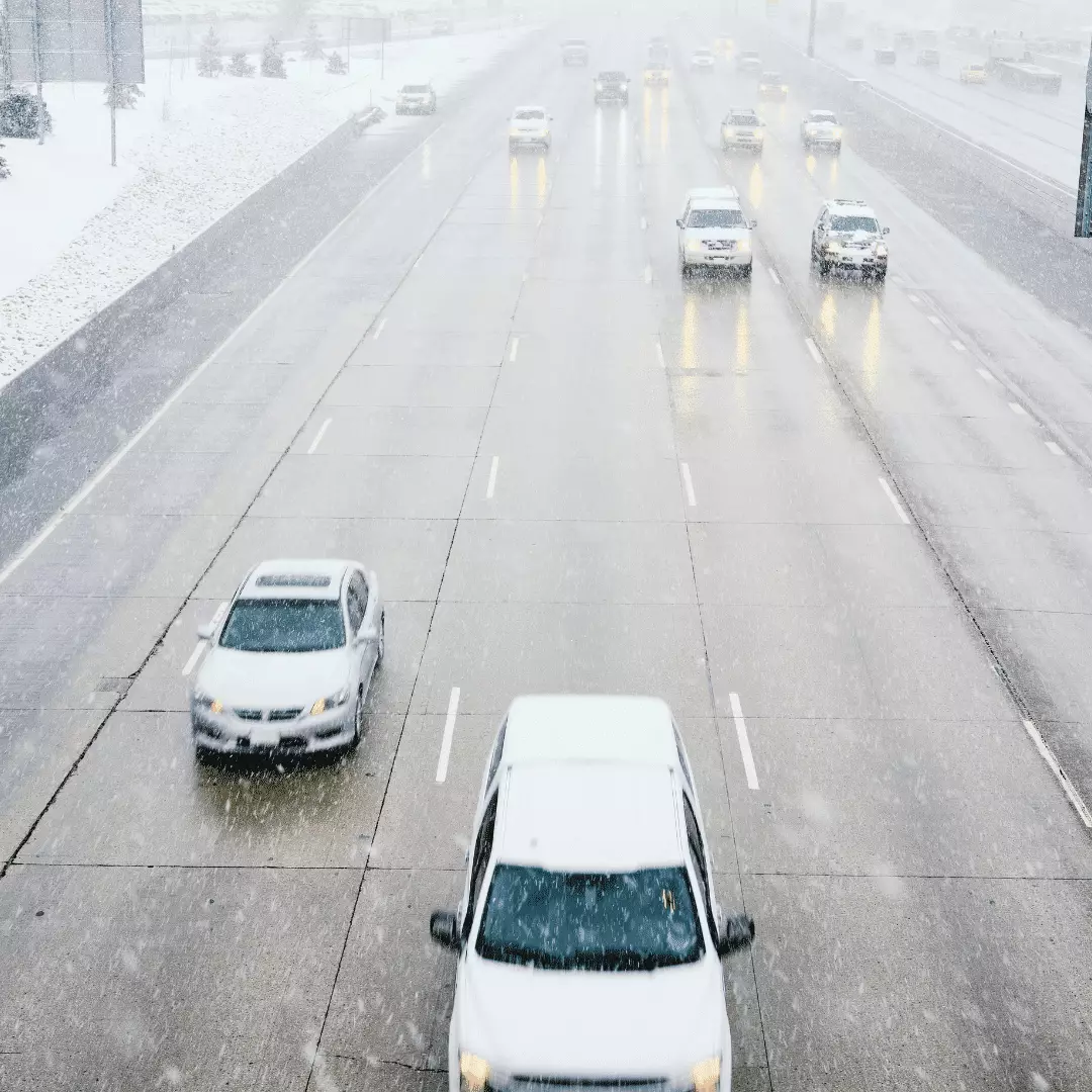 Vehicles navigating hazardous, snow-covered highway conditions during a winter storm.